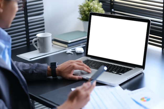 Homem de negócios cortado segurando um telefone celular e verificando informações na tela do laptop