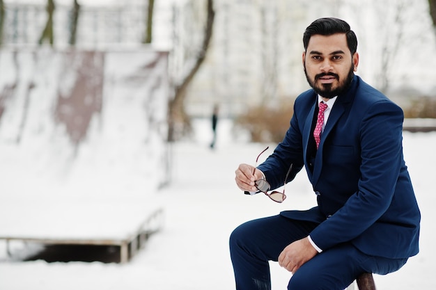 Homem de negócios de barba indiana elegante de terno e óculos de sol posou no dia de inverno ao ar livre