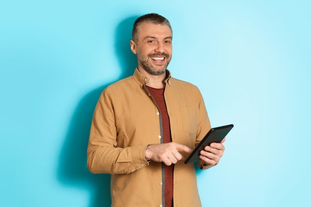 Homem de negócios de meia idade usando tablet digital sobre fundo azul