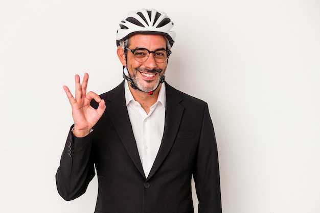 Homem de negócios de meia idade usando um capacete de bicicleta isolado em fundo azul alegre e confiante, mostrando o gesto okey