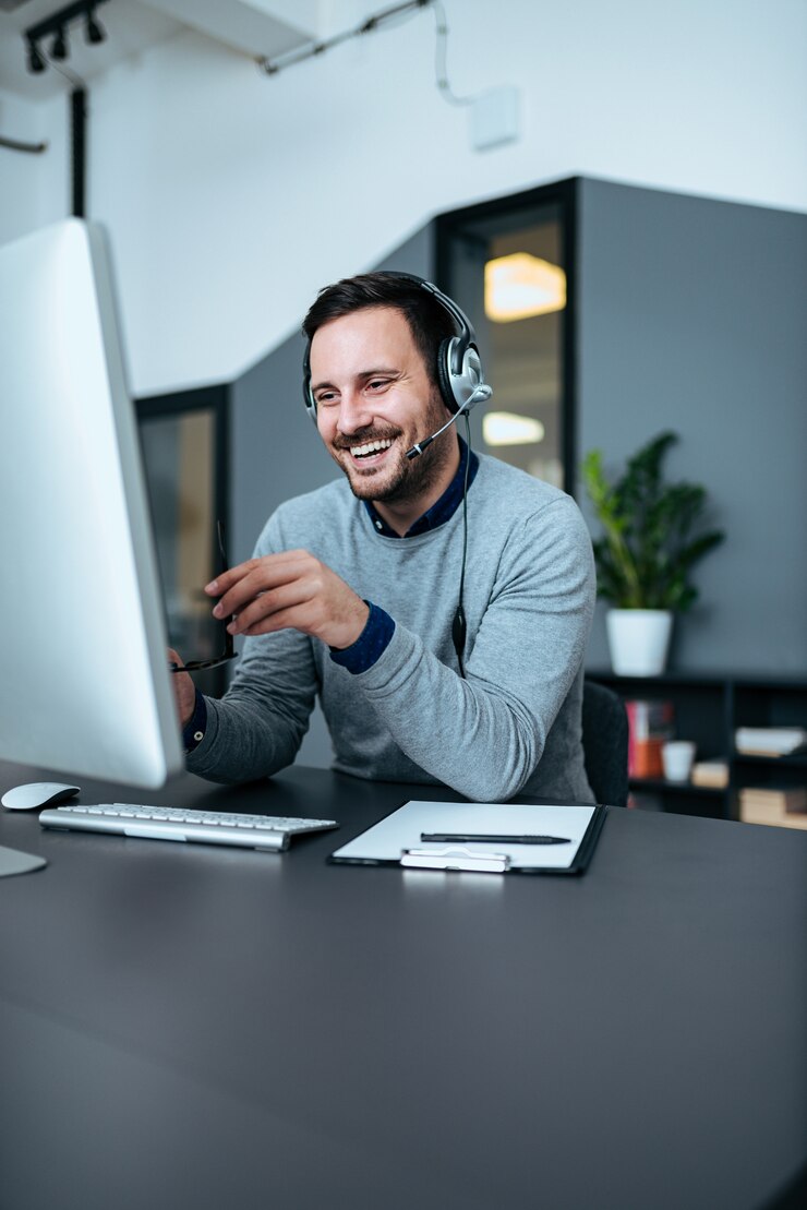 Homem de negócios de sorriso ocasional com os auriculares no trabalho no escritório moderno. Copie o espaço.
