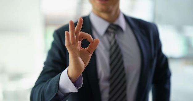 Homem de negócios de terno mostrando gesto de mão ok no trabalho em close-up do escritório