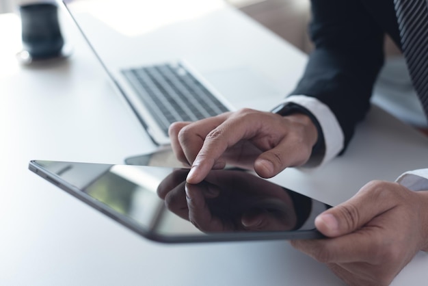 Homem de negócios de terno preto usando tablet digital na mesa no escritório Homem de negócio tocando o dedo no tablet de tela em branco online trabalhando com computador portátil na mesa do escritório em close-up