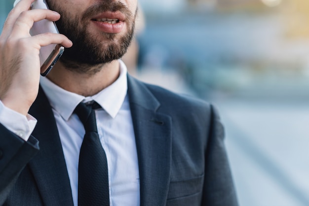 Foto homem de negócios do close-up que fala no smartphone contra o negócio que constrói fora.