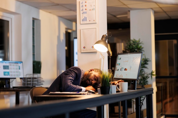 Homem de negócios durmindo na mesa por causa do excesso de trabalho no escritório da startup gerente executivo viciado em trabalho adormecendo depois de trabalhar até tarde da noite no plano de investimento da empresa conceito de negócio