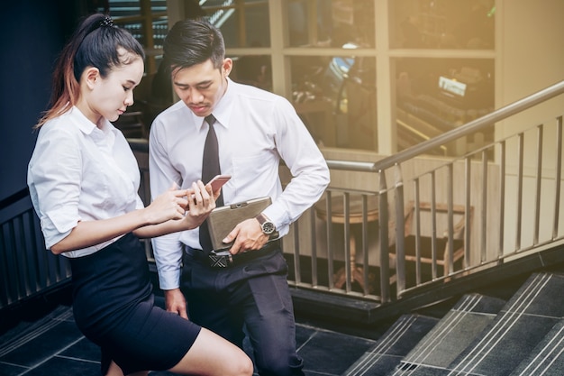Homem de negócios e mulher Usando smartphone em pé conversando e visualizando documentos ao ar livre
