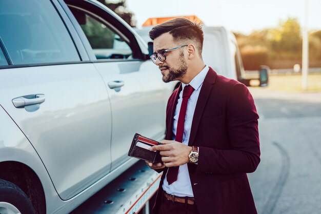 Homem de negócios elegante de meia-idade usando o serviço de reboque para socorrer o acidente de carro na estrada. conceito de assistência na estrada.