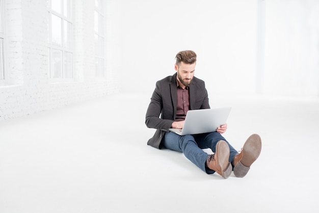 Homem de negócios elegante trabalhando com o laptop no chão no interior do grande escritório branco