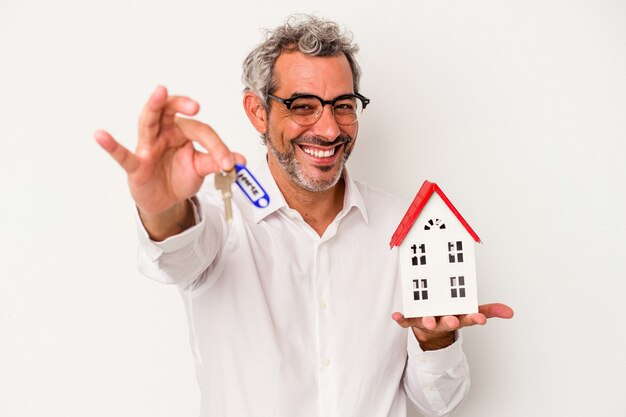 Homem de negócios em idade ociosa segurando as chaves e a casa do brinquedo isolada sobre fundo azul