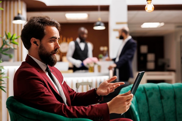 Homem de negócios em reunião de videoconferência usando tablet para conexão à internet enquanto espera o processo de check-in Empresário em viagem de negócios para o exterior, teleconferência remota.