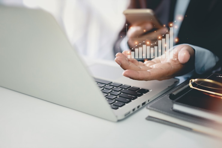 Foto homem de negócios em terno preto sentado e trabalhando no computador e telefone móvel. as mãos do homem mostrando sucesso e crescimento dos negócios resultam em diagrama de gráfico virtual com plano de crescimento futuro.