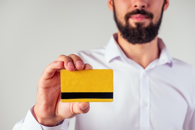 Homem de negócios em uma camisa branca segurando o cartão de crédito amarelo olhando para a câmera sorrindo venda de sexta-feira negra e gastar o conceito de dinheiro