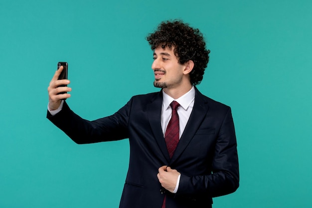 Homem de negócios encaracolado bonitão de terno preto e gravata vermelha tomando selfie no celular
