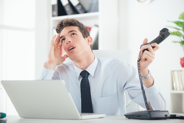 Homem de negócios entediado trabalhando no escritório, segurando o telefone e pensando.