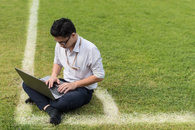 homem de negócios está sentado trabalhando com computador laptop no campo de futebol. conceito de trabalho