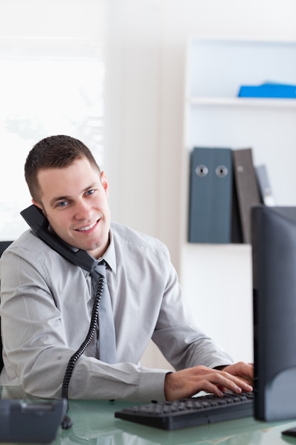 Homem de negócios falando ao telefone enquanto usa seu computador