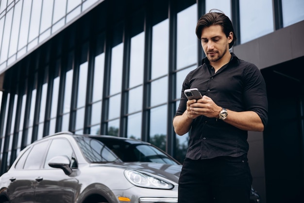 Homem de negócios falando ao telefone por seu carro perto do prédio de escritórios