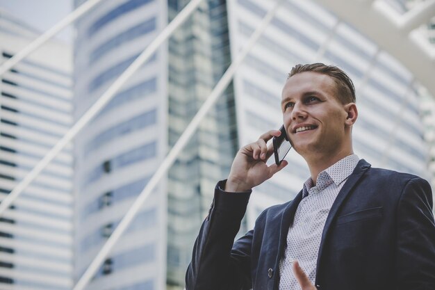 Homem de negócios falando em telefone inteligente enquanto estava de pé contra um edifício na cidade