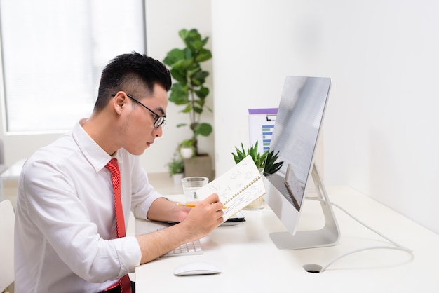 Homem de negócios feliz com o livro na mão, olhando para o monitor do computador no escritório