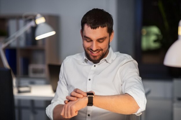 Foto homem de negócios feliz com relógio inteligente no escritório de noite