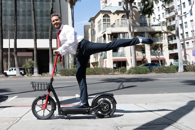 Homem de negócios feliz em terno montando scooter eletro ao ar livre no meio urbano da paisagem urbana, transporte de aluguel.