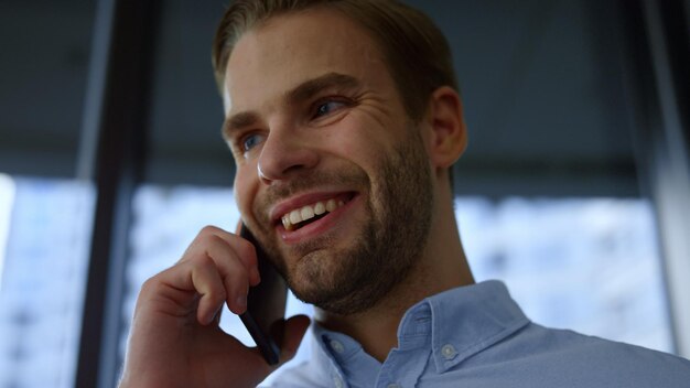 Homem de negócios feliz falando no celular no escritório Closeup trabalhador corporativo usando smartphone Retrato sorridente empresário conversando ao telefone Jovem chamando o telefone com emoção positiva