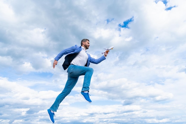 Homem de negócios feliz na jaqueta segurar avião de brinquedo no fundo do céu correr para o sucesso, realização.