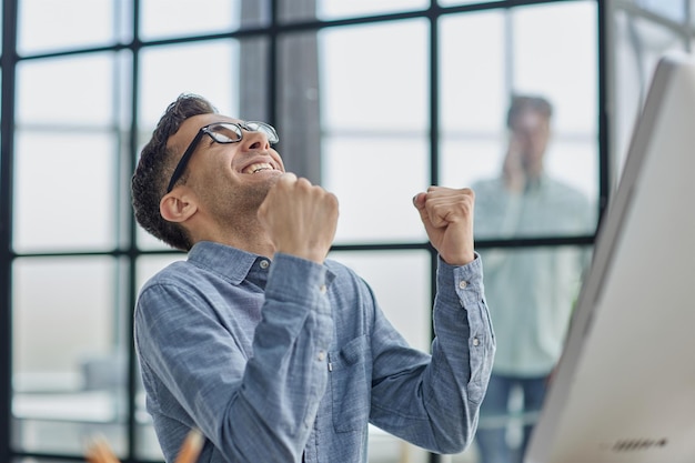 Homem de negócios feliz regozijando-se com o sucesso no local de trabalho no escritório olhando para a tela do laptop com expressão euforica