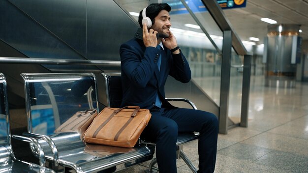 Foto homem de negócios habilidoso ouvindo música enquanto está sentado na estação de trem exultante