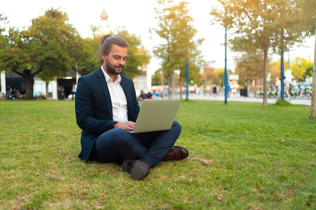 Homem de negócios hispânico bonito sentado em posição de lótus no parque público usa laptop