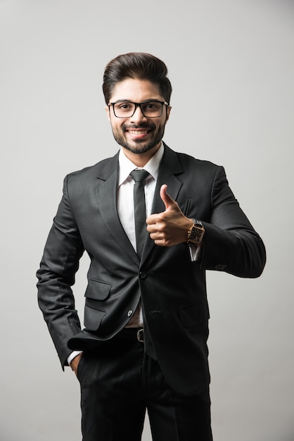 Foto homem de negócios indiano barbudo comemorando o sucesso com o polegar para cima ou levantando o punho em pé isolado sobre um fundo preto