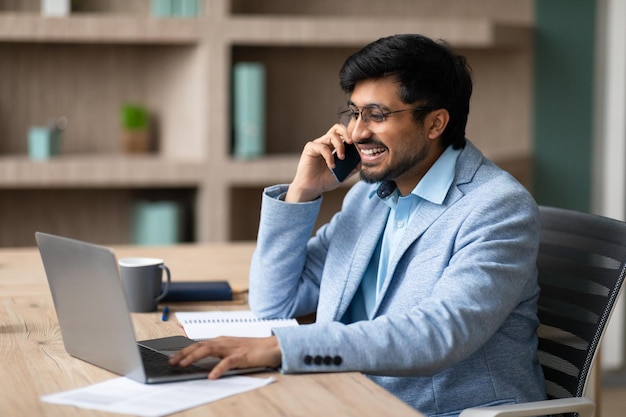 Homem de negócios indiano envolvido em conversa por telefone trabalhando online em ambientes fechados