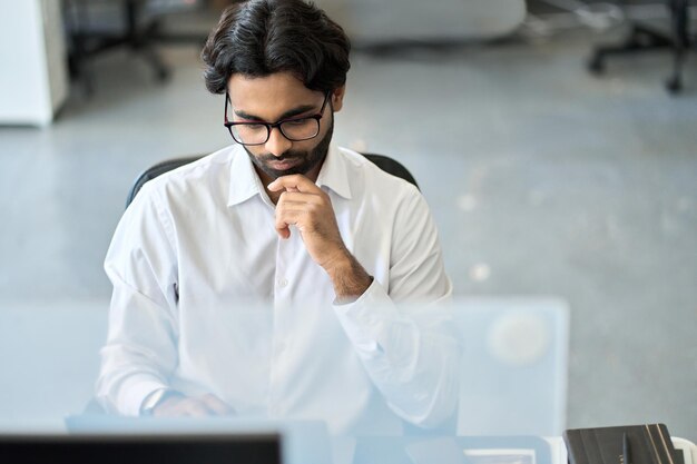 Homem de negócios indiano sério ocupado analisando dados de mercado olhando para o computador