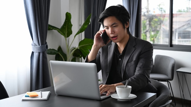 Homem de negócios inteligente falando no celular e usando o laptop no escritório.