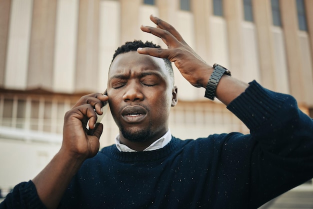 Homem de negócios irritado e estressado cansado falando em um telefonema irritante ao ar livre em uma cidade Dor frustrada ou empresário negro doente com dor de cabeça ou enxaqueca fora de uma cidade urbana