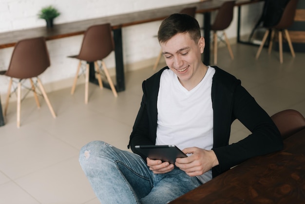 Homem de negócios jovem alegre vestindo roupas de moda casual senta-se à mesa e usa tablet Freelancer relaxado trabalhando em home office sentado em uma mesa com tablet digital