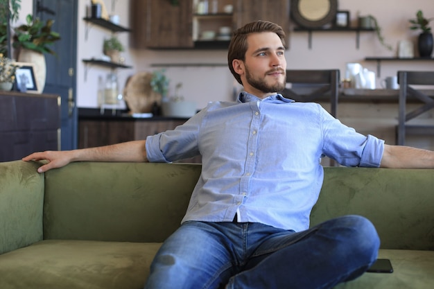 Homem de negócios jovem bonito parece relaxado enquanto está sentado no sofá em casa.