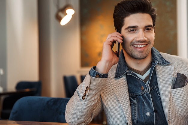 homem de negócios jovem bonito posando dentro de casa no escritório, falando pelo telefone celular.