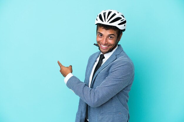 Homem de negócios jovem brasileiro com capacete de bicicleta isolado em fundo azul, apontando para trás