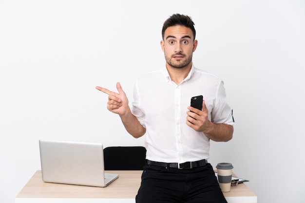 Homem de negócios jovem com um telefone móvel em um local de trabalho apontando para as laterais tendo dúvidas