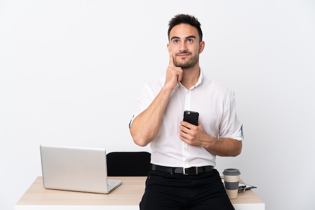 Homem de negócios jovem com um telefone móvel em um local de trabalho, pensando em uma idéia