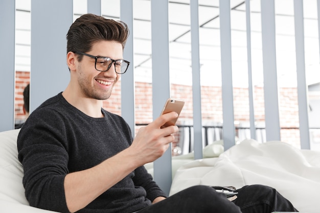 Homem de negócios jovem confiante trabalhando no escritório enquanto está sentado em um sofá, falando no celular