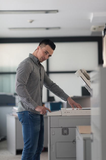 Foto homem de negócios jovem copia documentos na máquina copiadora no interior do escritório de inicialização moderno, roupas casuais