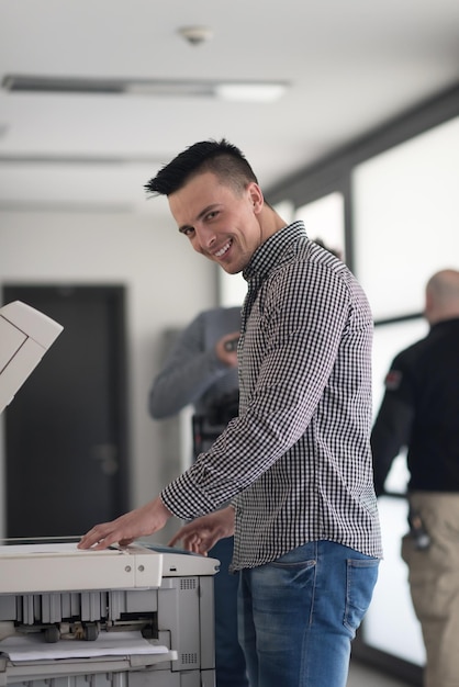 Foto homem de negócios jovem copia documentos na máquina copiadora no interior do escritório de inicialização moderno, roupas casuais