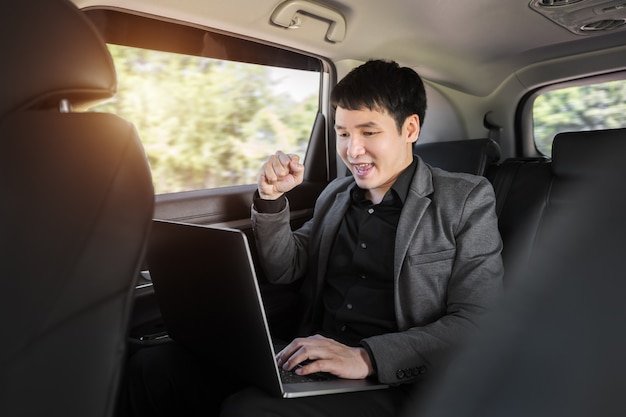 Homem de negócios jovem de sucesso usando um laptop enquanto está sentado no banco de trás do carro