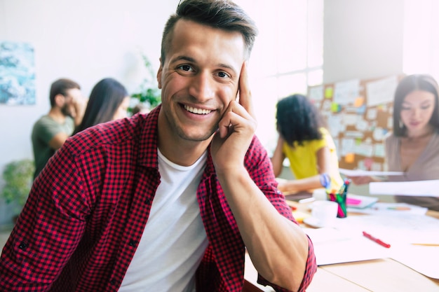 Homem de negócios jovem e bonito e moderno, com roupas casuais inteligentes, está na frente de uma equipe de negócios bem-sucedida que trabalha com gráficos e documentos