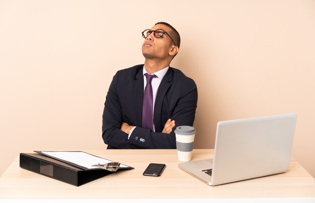 Homem de negócios jovem em seu escritório com um laptop e outros documentos fazendo dúvidas gesto enquanto levanta os ombros