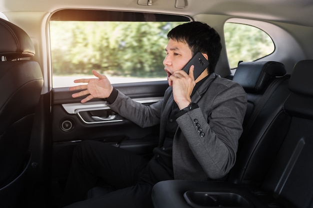 Homem de negócios jovem estressado falando sobre o problema em um telefone celular enquanto está sentado no banco de trás do carro