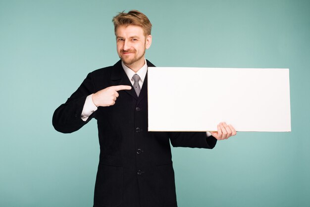 Homem de negócios jovem feliz e sorridente aponta a tabuleta em branco, azul