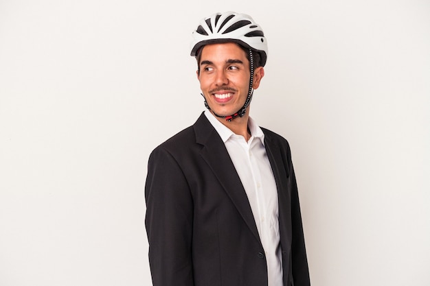 Homem de negócios jovem raça mista usando um capacete de bicicleta isolado no fundo branco parece de lado sorrindo, alegre e agradável.